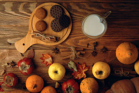 Chocolate cookies, vegetables, fruit and milk in a mug in the shape of a heart. Baking with cinnamon sticks on a wooden background. Autumn composition. Apples and persimmons, fall harvest.の写真素材