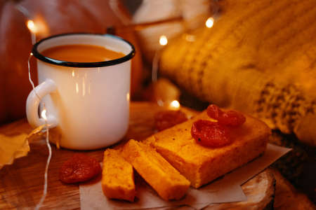 Cute festive composition with lights. Photos for making cards and invitations for Christmas and thanksgiving. Pie, pumpkin juice, dried apricots on wooden tray. A knitted sweater and a ripe pumpkin.の写真素材