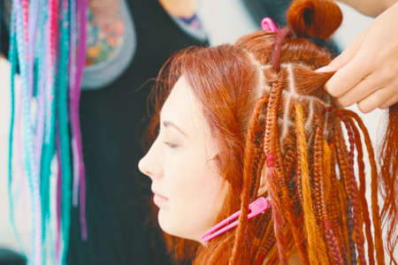 Cool hairstyle made of artificial hair. Barber braids dreadlocks. Hairdresser weaves braids with kanekalon to young girl head, making creative hairstyle with thick plaits.の写真素材
