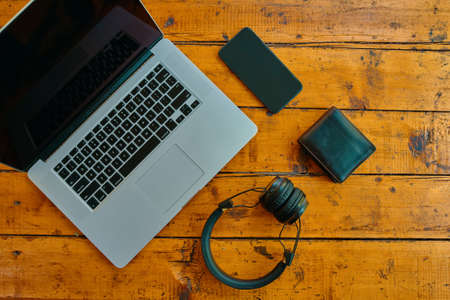 Laptop, wireless headphones, mobile phone, and wallet on wooden table. Modern devices for business jobs and entertainment. Freelancers work surface. Black cell phone screen to insert some text.の写真素材