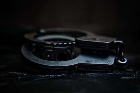 Handcuffs and the muzzle of hand gun close up. Firearms and tools for apprehending criminals on black table. Police ammunition.の写真素材