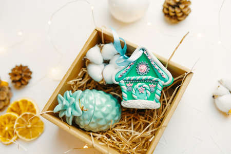 Christmas gift box with gingerbread house and candle. Festive souvenir made of polymer clay. New Years surprise, cones and dried oranges on white table. Composition for design of greeting postcards.の写真素材