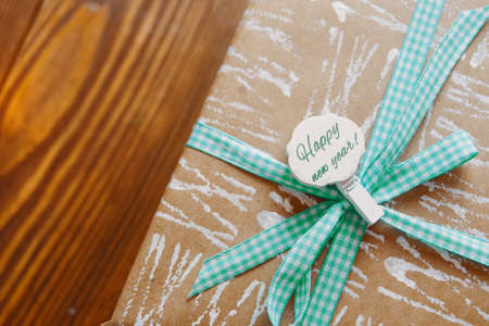 Gift box wrapped in craft paper with checkered ribbon on wooden table. Decorative clothespin with inscription Happy New Year. Winter holiday. Packaging of Christmas gifts.の写真素材