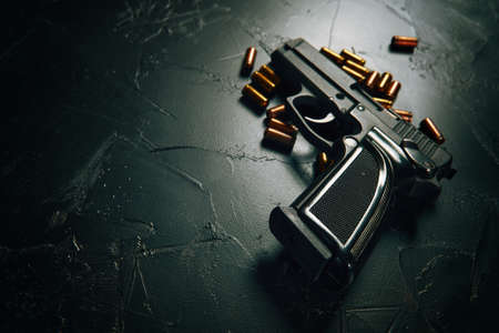 Pistol with bullets on concrete table. Black gun and brass cartridges. Firearms close-up. Weapon of crime. Means of defense or attack. Copy space for text.の写真素材