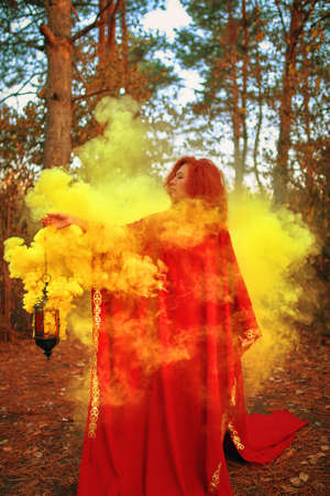 Smoke screen in the woods. Red hair woman wearing dress surrounded by smoke. In the forestの写真素材