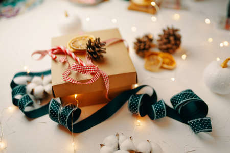 Christmas gift and decorations on white textured table. Festive still life. Cardboard box, colorful ribbons, garlands, dried orange slices and cones. New Years atmosphere. Wintertime.の写真素材
