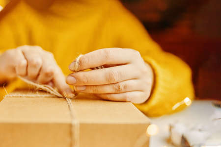 Girl in orange sweater ties string on box. Packaging of gifts for holiday.の写真素材