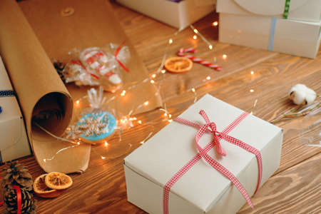 Christmas gift with red ribbon, gingerbread, sweets, craft wrapping paper, pine cone and garlands on wooden table. Festive mood and holiday decorations. Surprise for New Year.の写真素材