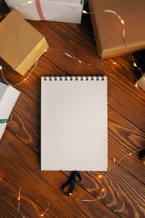 Flat lay of blank notebook garland and gift boxes on wood table background. Christmas New Year and birthday concept. Copy space for any design. Space for modern creative work of designer.の写真素材