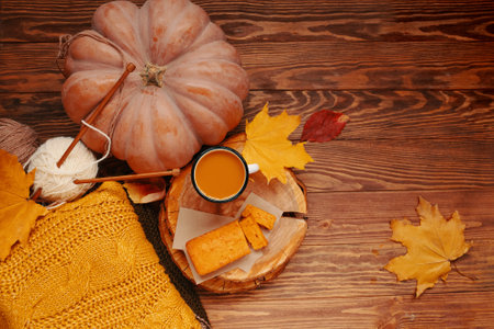Wooden tray with pumpkin pie and flavored coffee in white mug. Top view of autumn composition with orange and green yarn sweater, around pumpkin and fall leaves on wooden background.の写真素材