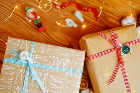 Top view of two Christmas gifts and decorations on wooden table. Nutcracker, lights of garlands, ribbons and boxes in patterned wrapping paper. Pins with inscriptions on New Years surprises.の写真素材