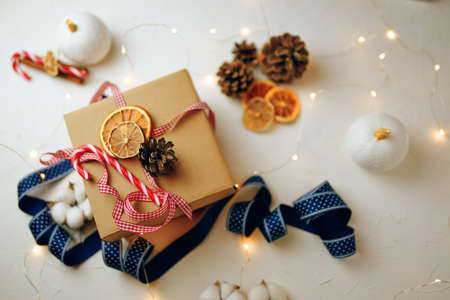 Top view of christmas gift box and decorations on white textured table. Candy cane, colorful ribbons, garlands, dried orange slices and cones. New Years atmosphere. Wintertime. Festive still life.の写真素材