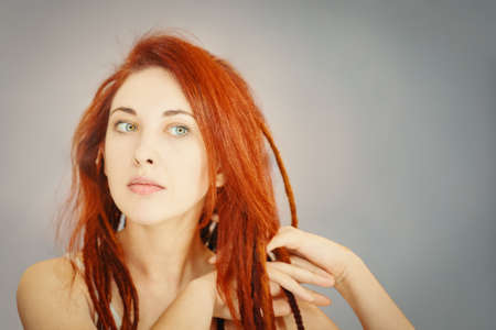 Red-haired girl combs her dreadlocks with fingers. Boho or hippie hairstyle. Woman with pigtails...
