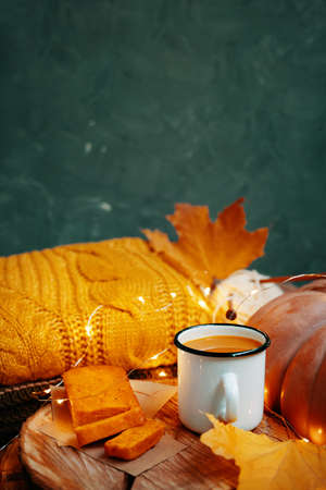 Autumn composition with a green background for Thanksgiving cards. Cocoa in a tin Cup and sweet freshly baked pumpkin and carrot cake on a wooden stand. Orange knitted sweater and yellow fall leaves.の写真素材