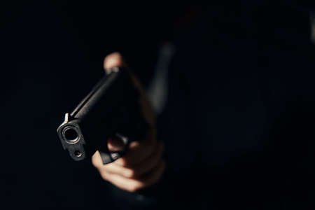 Gun in mans hand on dark background. Firearms close-up. Pistol for attack or defense. Criminal concept.の写真素材