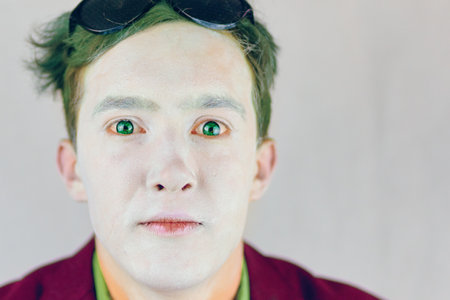 Guy with white makeup on face and green hair. Greasepaint of clown or mime. Man actor in suit looks...