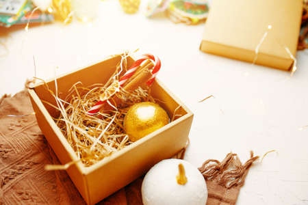 Close up of Christmas composition. Brown warm blanket and gift box with New Year golden ball, lollipops and cinnamon sticks on white table. Festive atmosphere.の写真素材