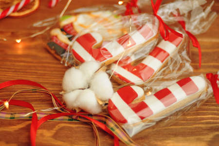Gingerbread in form of sugar canes on wooden table. Cookies with red and white icing in stripes. Christmas sweets in bags with ribbons.の写真素材