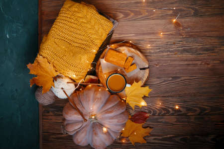 Top view of autumn composition for postcards. Pumpkin juice and sweet carrot cake on wooden tray. Ripe pumpkin and warm knitted sweater with ball of white yarn and fallen leaves on wooden background.の写真素材