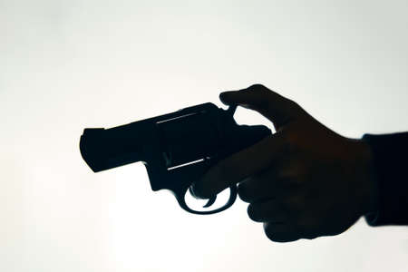 Silhouette of hand with gun on white background. Man pulls the trigger of revolver to fire. Criminal with pistol close up. Firearm for attack or defense.の写真素材