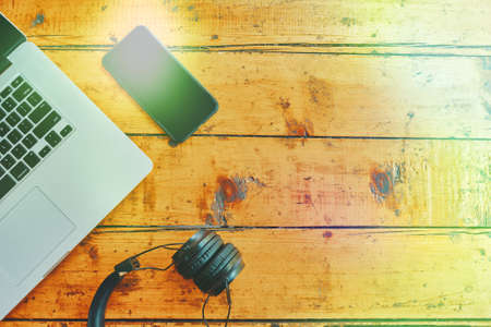 Laptop, wireless headphones and smartphone on wooden table with sunlight. Modern devices for business podcast and entertainment. Freelancers work surface. Top view with copy space.の写真素材