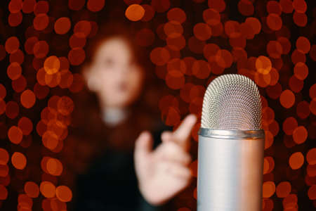 Close-up of retro microphone and silhouette of female singer on bokeh background. Woman pulls hand to disco mic for sing at concert.の写真素材