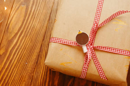 Gift box on wooden table. Craft wrapping paper with golden touches design and ribbon. Decorative clothespin in shape of Christmas ball with place for inscription. Concept of Christmas and New year.の写真素材