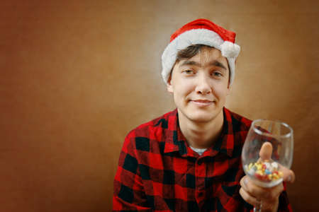 Guy in Santa Claus hat holds a glass with various pills and drugs. Fighting the coronavirus on...
