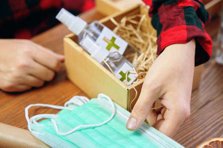 Mens hands take medical masks to put them in a gift box with antiseptics. Gift in quarantine on a...