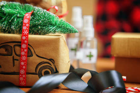 Christmas present with painted car carrying Christmas tree on the roof. Christmas ribbon and antiseptics on background. Lollipops on a wooden table. New Years atmosphere. Quarantine holiday.の写真素材