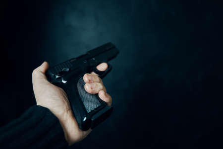 First person view of gun. Firearm in mans hand. Criminal with pistol on dark background. Defense or attack. Murderer or armed thief. Close up with copy space.の写真素材