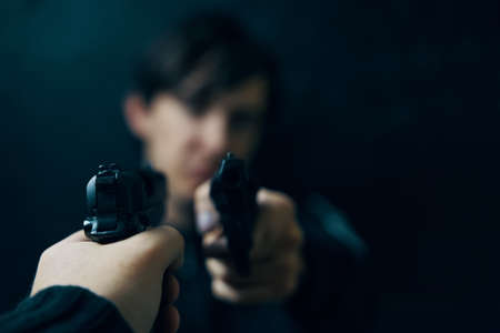 Close-up of mans hand with gun pointed at criminal with revolver. Shootout of two thieves or...
