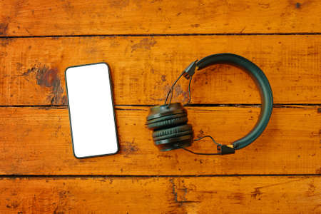 Headphones and smartphone on wooden table. Top view on mobile phone with empty screen.の写真素材