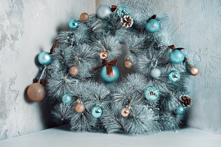 Round fir garland with snow, blue glitter balls and pine cones. Traditional Christmas decorative wreath over grey antique marble wall. Holiday interior details. New Year mood.の写真素材