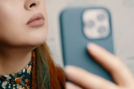 Red-haired girl with bright makeup takes a selfie on the camera of a modern phone. Blogger woman...