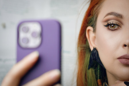 Red-haired girl takes selfie on front camera of smartphone. Female blogger runs a blog about fashion and makeup. Woman with Gothic-style jewelry with proud expression on her face. Witch aesthetic.の写真素材