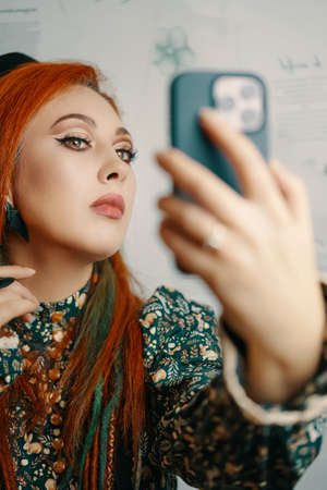 Adorable woman takes a selfie on the front camera of a modern smartphone. Female blogger shoots...