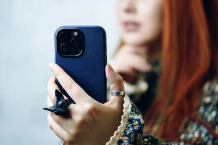 Females hand with gothic ring holding smartphone in blue case. Woman blogger takes selfie on iPhone 13 pro. Focus on foreground. Gadget with triple-lens camera. Bishkek, Kyrgyzstan - January 24, 2022のeditorial素材