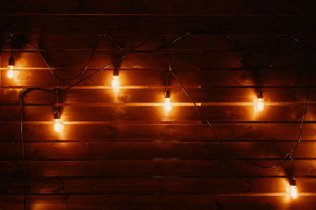 Vintage hanging incandescent lamps on wires. Wooden wall with light bulbs. Loft party interior. Rustic background with copy space. Scene decoration for country festival.の写真素材