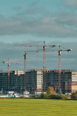 Construction site with industrial building cranes, multi-storey buildings of new city districts and large green field. Project of urban area. Blue sky with clouds.の写真素材