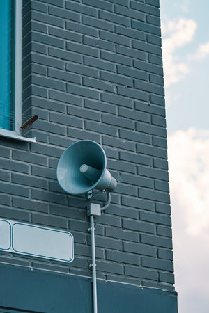 Megaphone hanging on apartment building. City hazard warning system. Loud speaker on brick wall with...