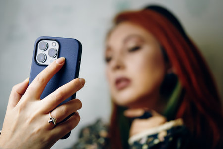 Close-up of womans hand with mushrooms ring holding smartphone in blue case. Red hair female takes selfie on iPhone 13 pro. Gadget with triple-lens camera. Bishkek, Kyrgyzstan - January 24, 2022のeditorial素材