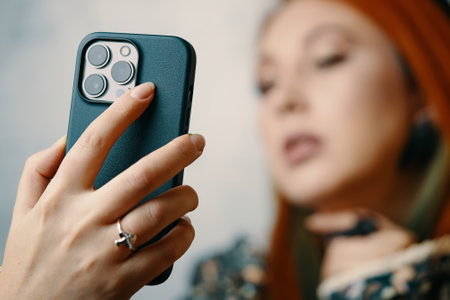 Fashionable female takes selfie on iPhone 13 pro. Gadget with triple-lens camera. Close-up of womans hand with mushrooms ring holding smartphone in case. Bishkek, Kyrgyzstan - January 24, 2022のeditorial素材