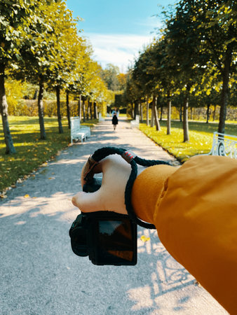 In a park, amidst trees, a man photographs a girl walking on a path, showcasing a first-person...