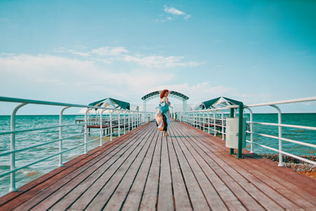 The resort pier comes alive with the presence of a woman sporting vibrant red hair, adorned in a summer dress, and carrying a backpack, enjoying a casual walk against the backdrop of the sea.の写真素材