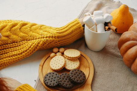 Cozy autumn scene with biscuits, marshmallows, yellow sweater, and pumpkins, offering a warm and inviting feelの写真素材