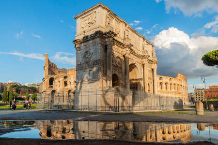 Arch of Constantine near the Colosseum and the Arch of Titus. Photographed after the storm, reflecting in a puddle with few tourists, blue sky and clouds. Rome.のeditorial素材