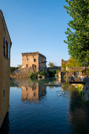 The beautiful medieval village of Borghetto di Valeggio sul Mincio. Detail of the medieval tower river with the bridge, the swans, the flowers and the medieval buildings. Verona, Veneto, Italyのeditorial素材