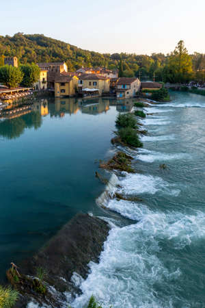 Panorama from the top of the medieval tower on the Mincio river with the waterfalls and the medieval village of Valeggio sul Mincio on a summer day, towards sunset. Verona, Veneto, Italyの写真素材