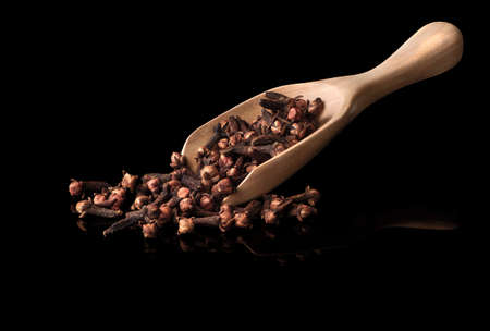 dried cloves in the wooden spoon, isolated on black  backgroundの写真素材